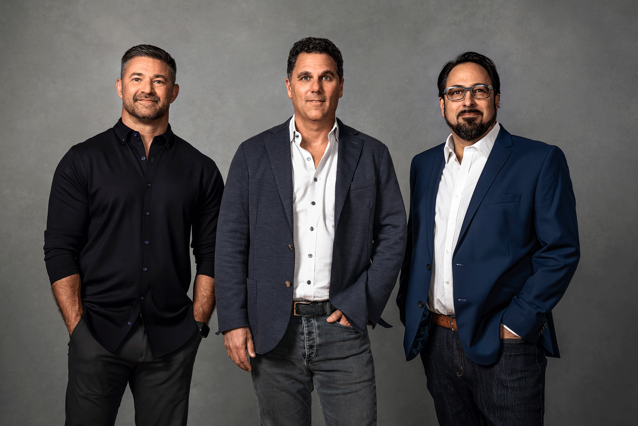 three men stand together against a grey background